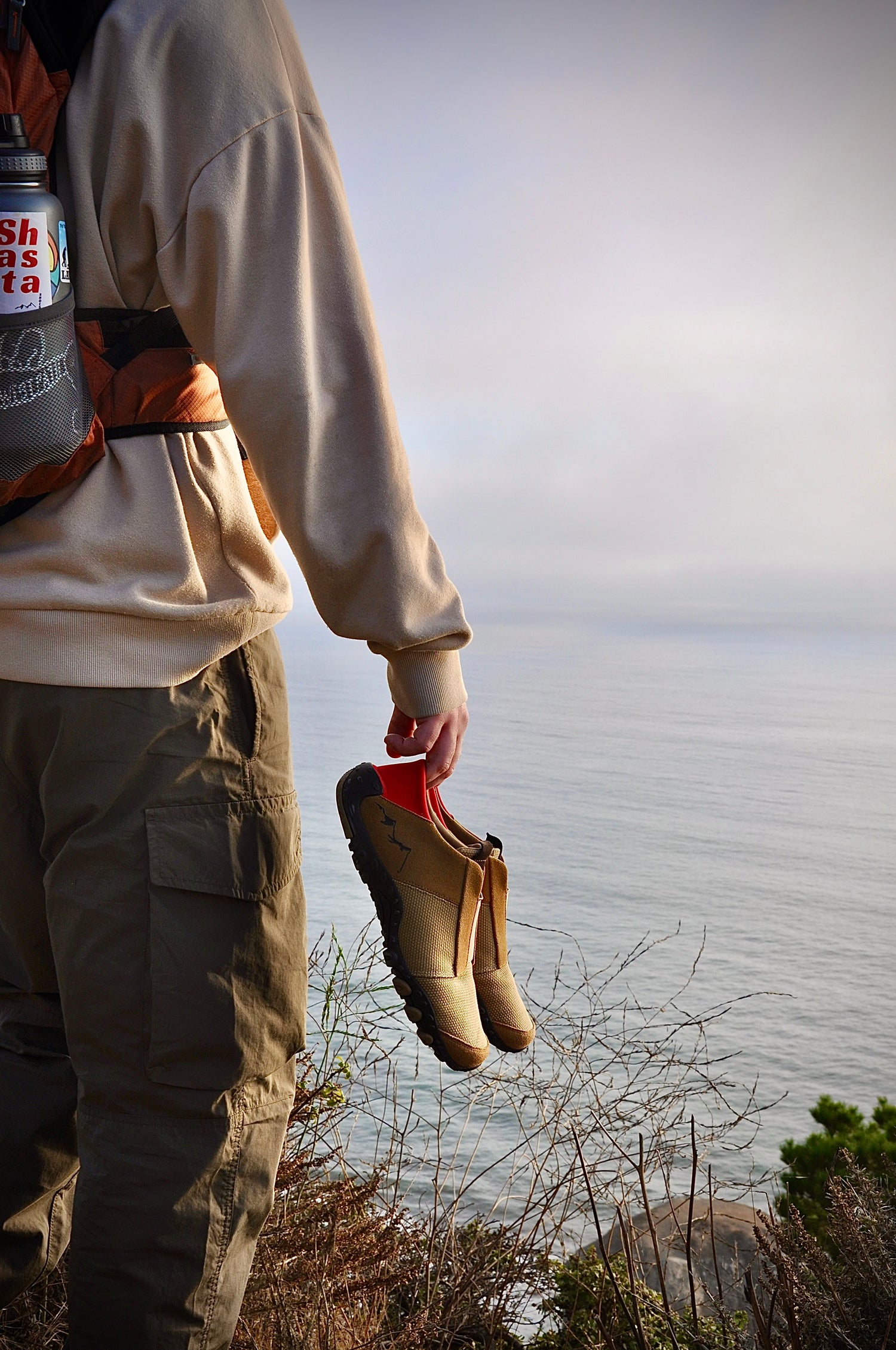 Holding Base Camp Shoes overlooking the water